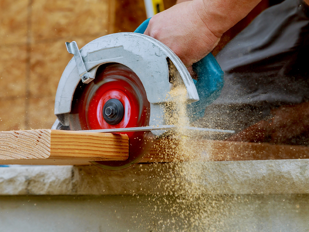 New home construction project building contractor worker using hand held worm drive circular saw to cut boards