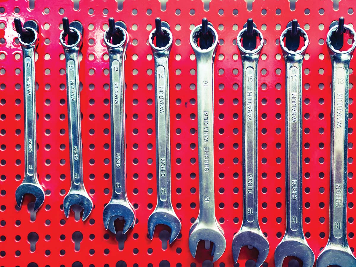 Different sized wrenches hanging on a red board from small to large.