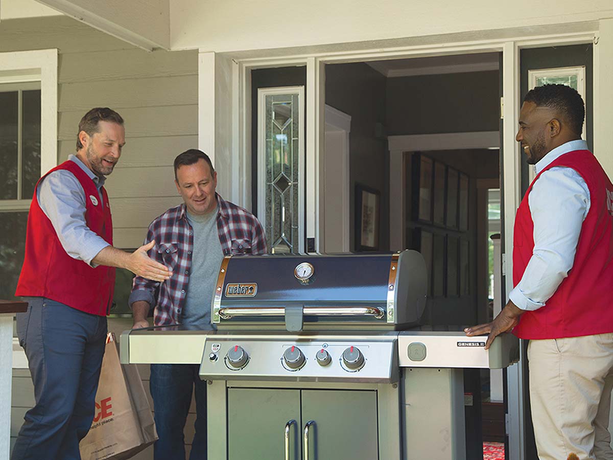 Two Ace Hardware employees deliver a new grill to a happy customer’s home.