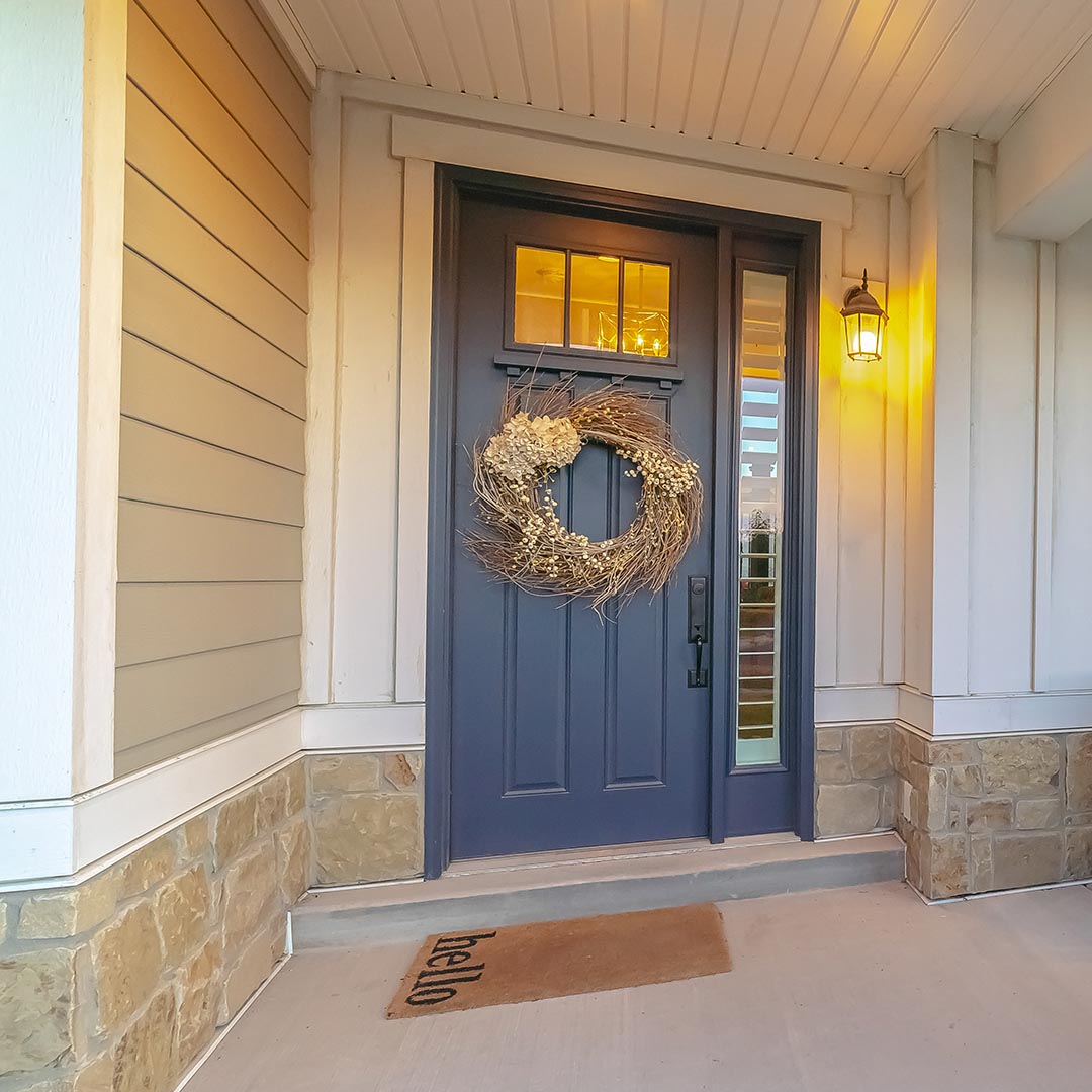 entryway with a gray door with a decorative wreath and a doormat